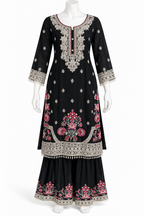 A black three-piece traditional Indian outfit displayed on a white mannequin, featuring a long kurta with pink floral embroidery, a matching flared sharara pant, and a wide border skirt with detailed silver and pink embroidery.