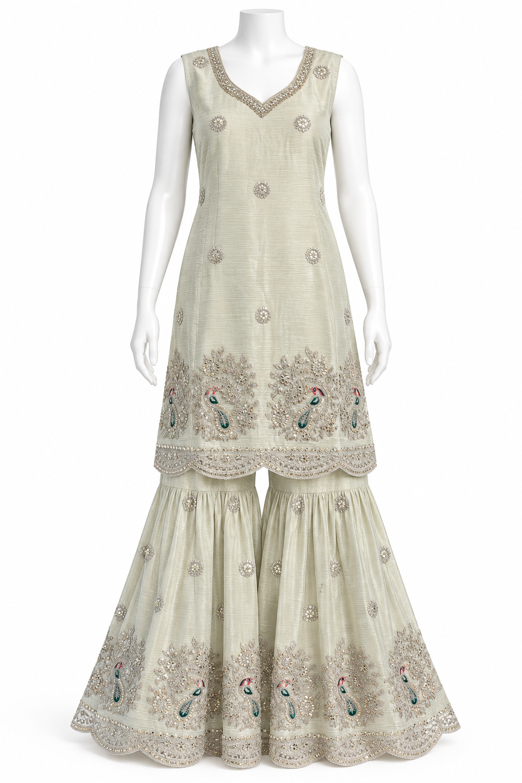 A sleeveless beige Anarkali kurta with matching flared sharara pants, displayed on a white mannequin. The outfit features intricate silver embroidery, a scalloped border, and peacock motifs with small blue and red accents near the hem.