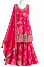A bright pink floral traditional outfit displayed on a white mannequin against a plain white background. The set includes a sleeveless embroidered top, matching flared skirt, and a sheer dupatta with decorative borders and tassels.