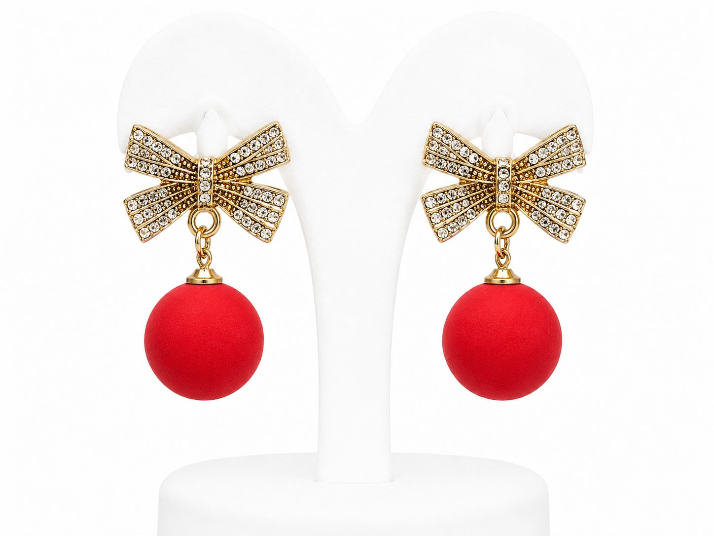 Pair of earrings with gold bows and red balls on a white background
