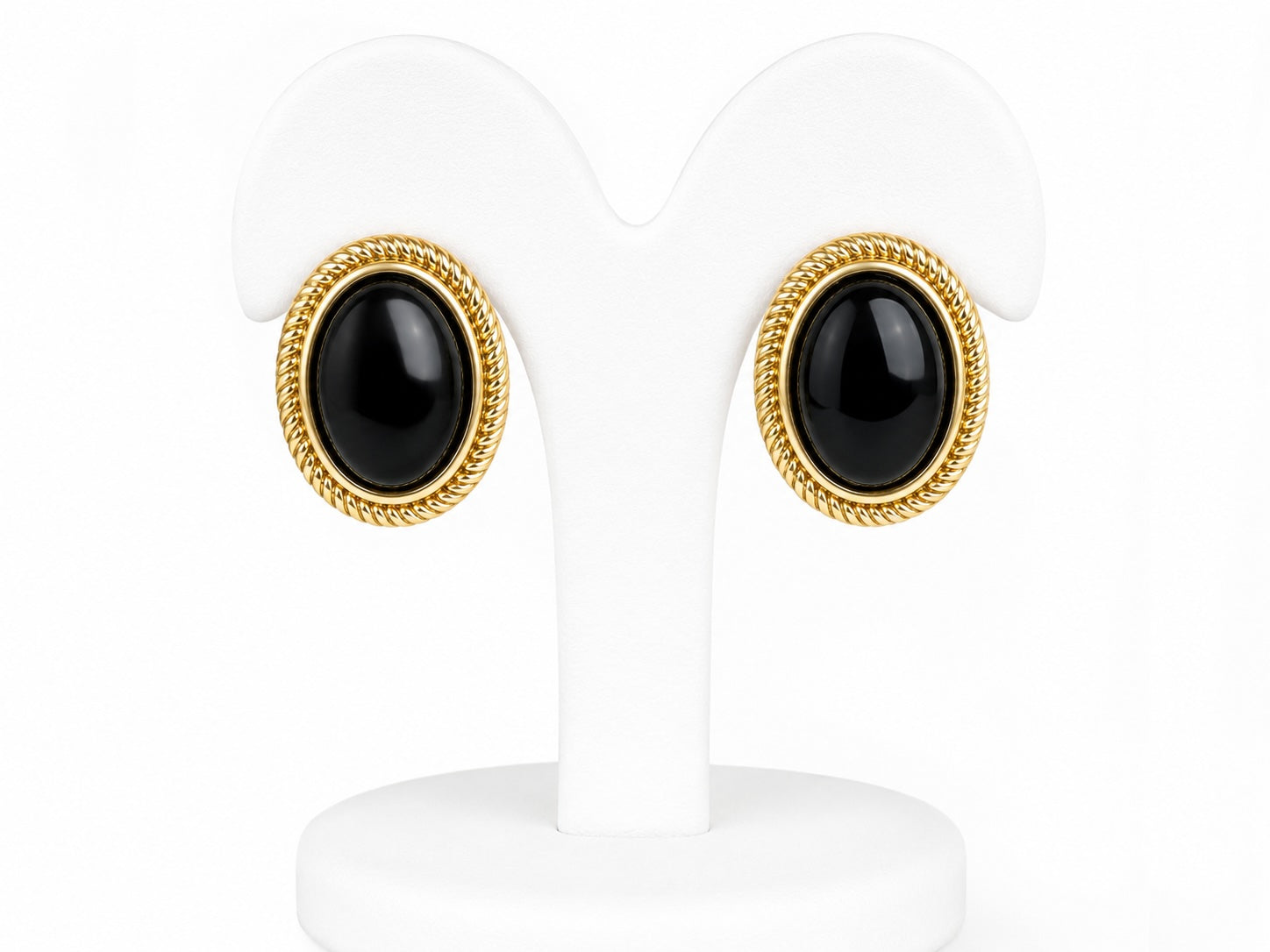 Pair of earrings with black stones and gold rims on white stands.