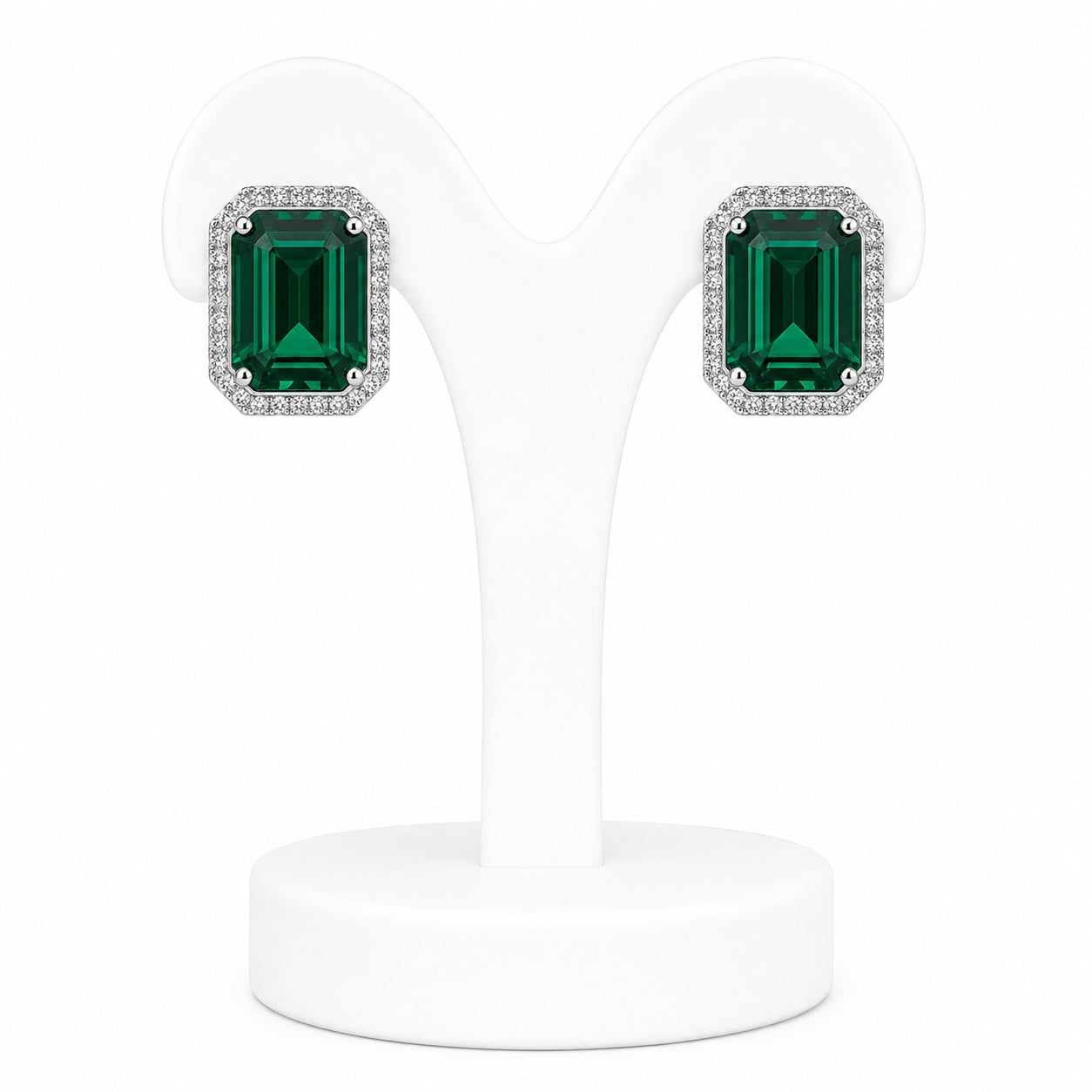 Pair of emerald green square gemstone earrings on a white stand.