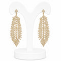 Gold leaf-shaped earrings on a white stand with a white background