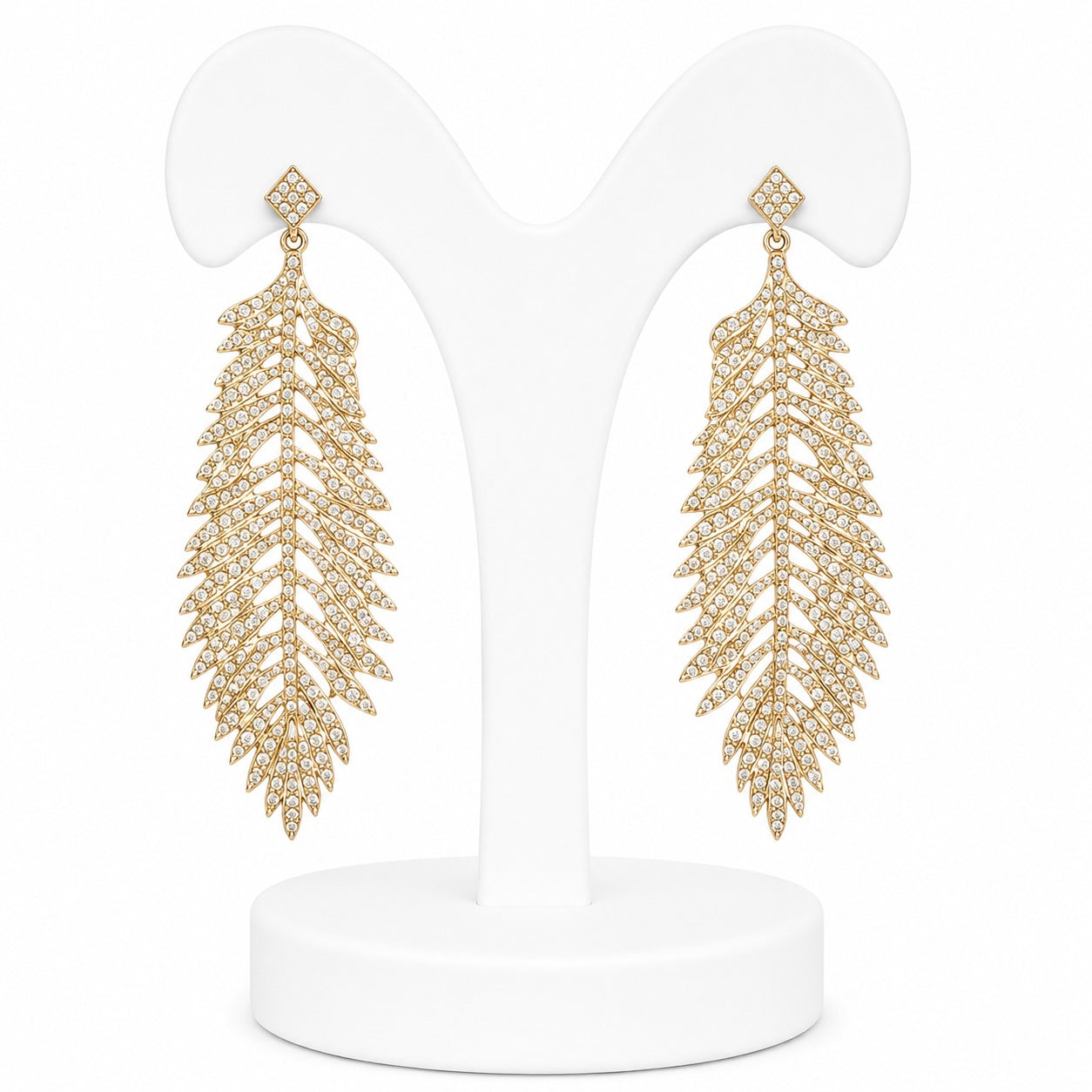 Gold leaf-shaped earrings on a white stand with a white background