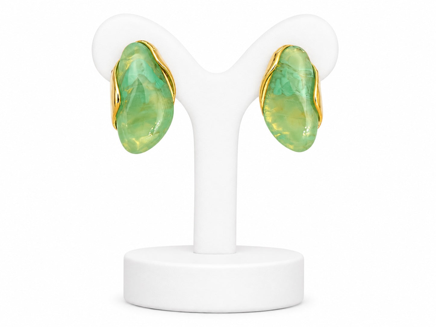 Pair of earrings with green stones and gold accents on a white stand.