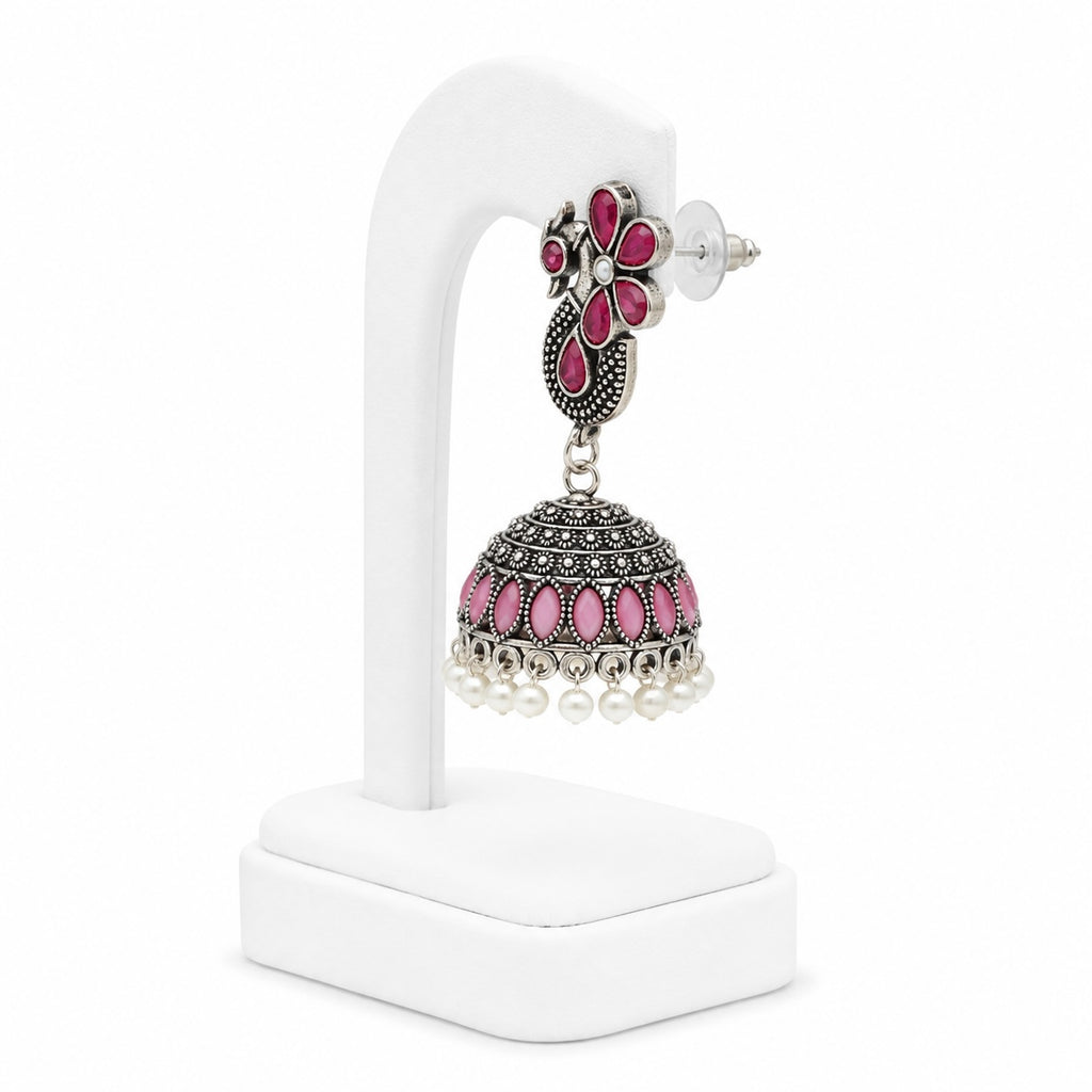 Ornate earring with pink stones and pearl-like beads on a white stand
