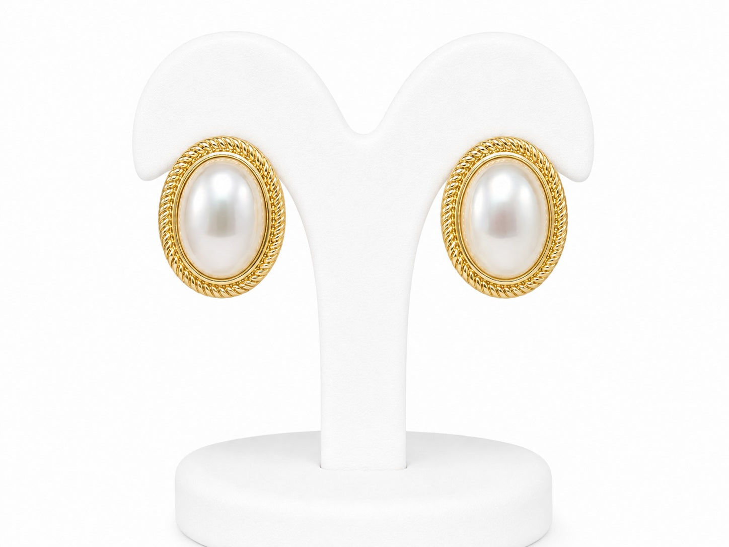 Pair of pearl earrings with gold accents on a white stand.