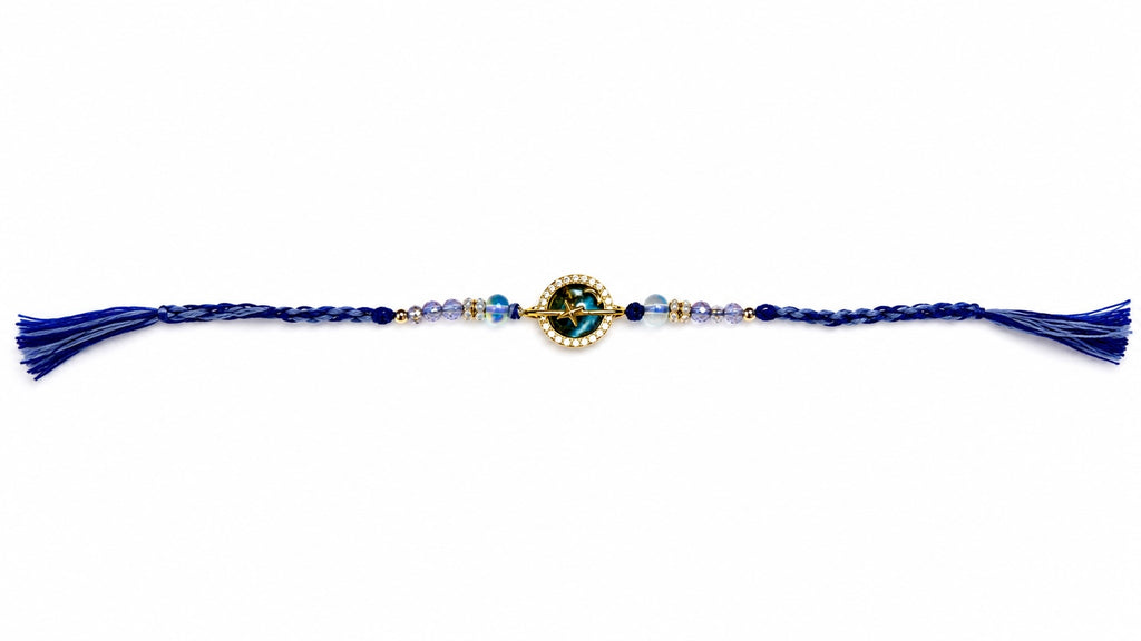A blue and gold beaded rakhi with braided ends and tassels, displayed horizontally on a plain white background.