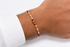A close-up of a person's wrist wearing a beaded bracelet with red cord, white pearl-like beads, and a central translucent amber bead, shown against a white background.