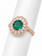 Rose gold ring with a green gemstone and clear stones on a white background