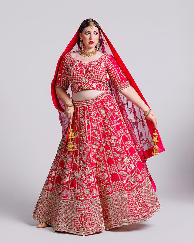 Woman wearing a red and gold traditional outfit with a dupatta on a light gray background